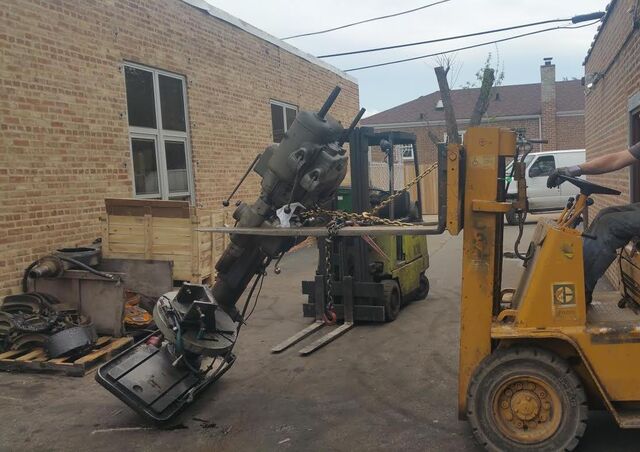 Two forklifts teaming up to lay a drill press down for transport